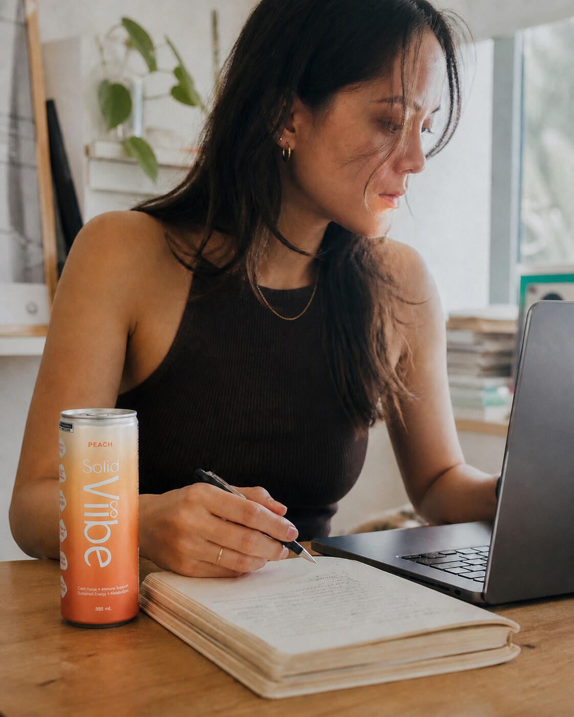 A woman working at an office desk in the afternoon, writing in a notebook beside an open can of Peach Solid Viibe