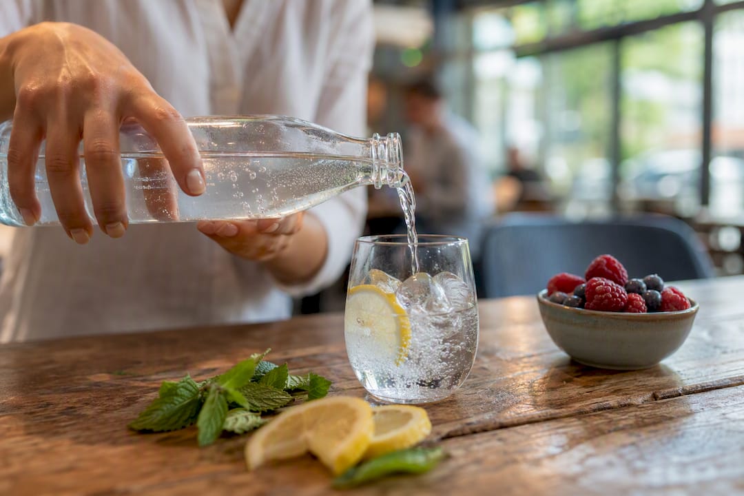 Hands pouring sparkling flavoured water with cucumber slice