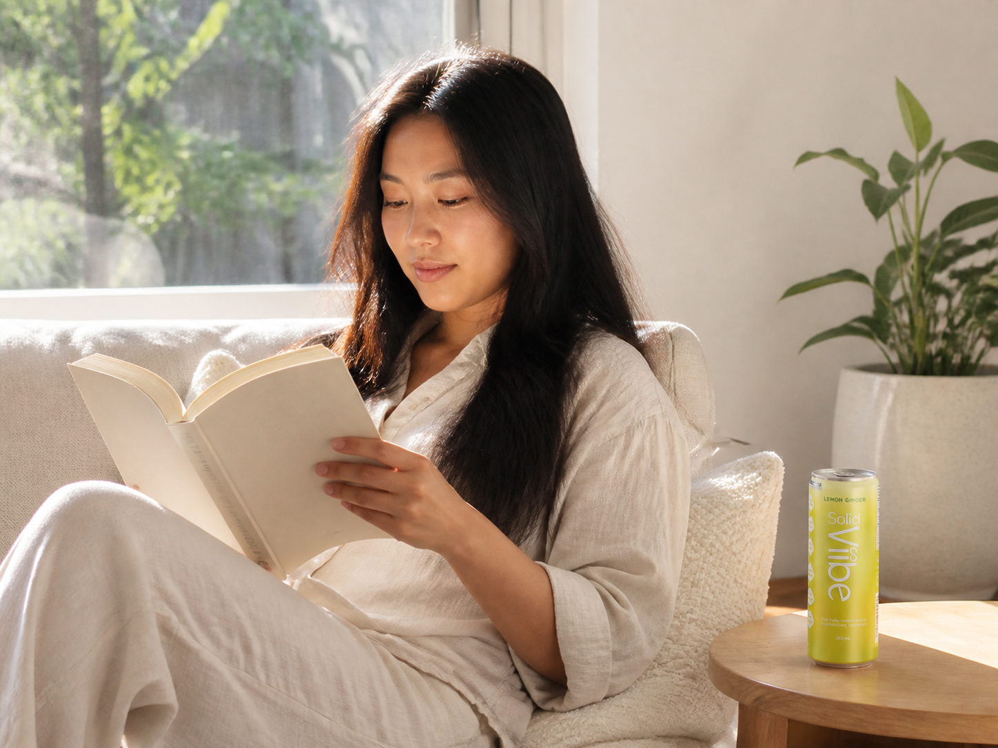 A woman reading on a sofa in soft afternoon daylight, an opened Lemon Ginger Solid Viibe on the side table beside her