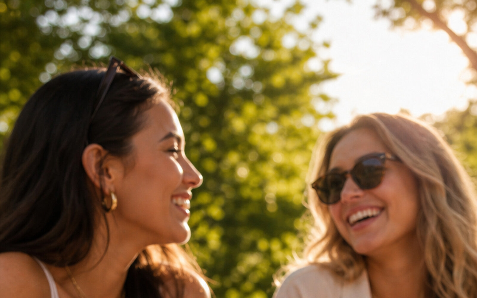 Two friends laughing together on a picnic blanket in a park on a sunny afternoon