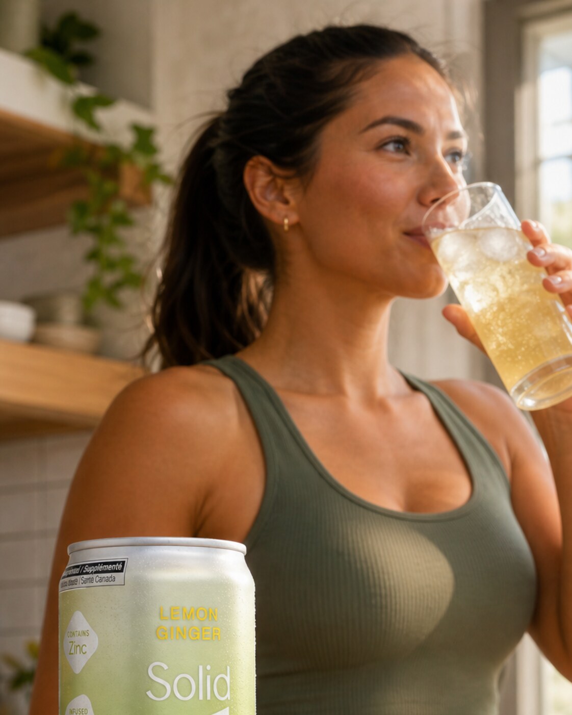A woman at a sunlit kitchen bench pouring a can of Lemon Ginger Solid Viibe into a tall glass of ice